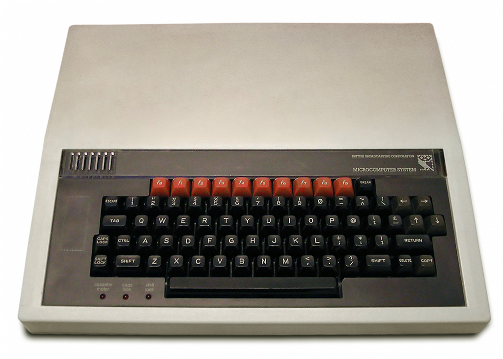 A BBC Micro computer - black keys built into a light beige plastic casing, with a row of red function keys above the keyboard.